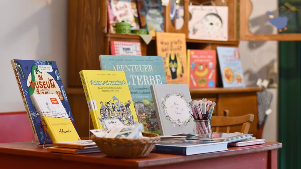 Bücher stehen auf einem Tisch, verschwommen im Hintergrund eine alte Holzvitrine mit Büchern