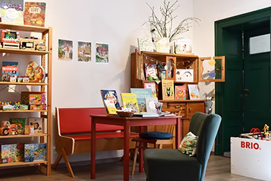 Tisch und Sessel mittig mit Bücherkommode im Hintergrund und Sachbuchregal links